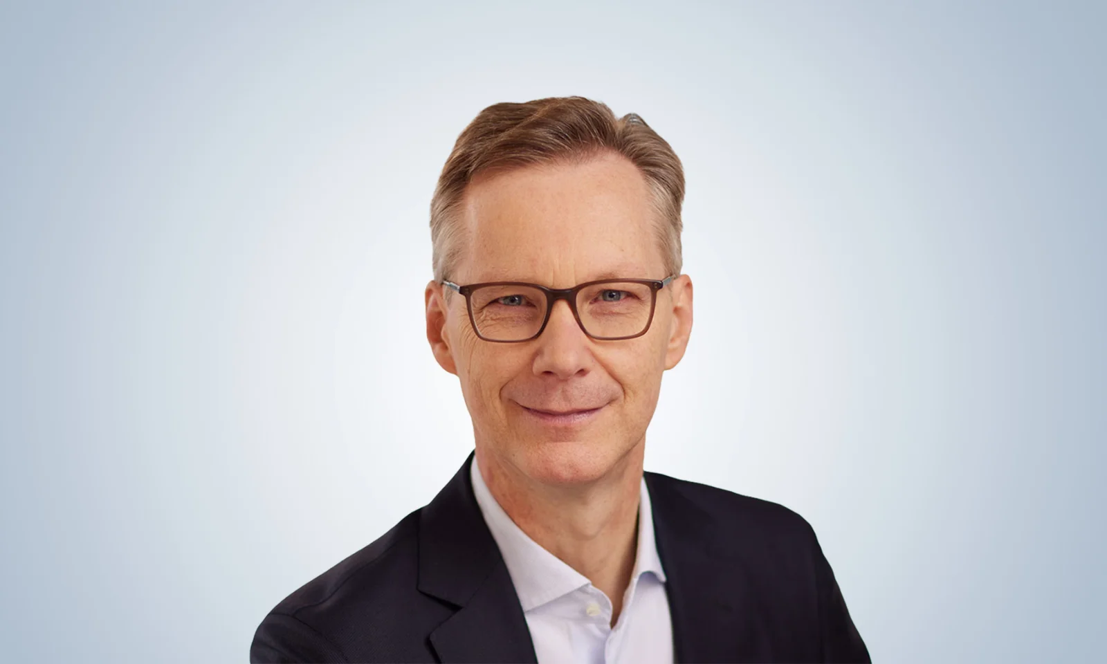 Professional portrait of a confident business leader wearing glasses, a dark blazer, and a light shirt against a gradient background.